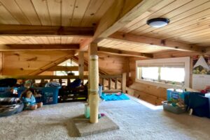 Cozy wooden loft on Just Wandering Lane with a carpeted floor, cat scratching post, toys, and baskets by a child.