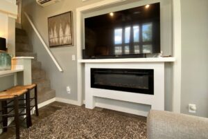 Wall-mounted TV above a modern fireplace on Just Wandering Lane, next to carpeted stairs and bar stools.
