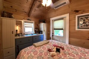Cozy wooden bedroom on Just Wandering Lane with a patterned bedspread, toys on the bed, and natural window light.