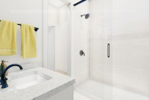 Bright bathroom with a white sink, black faucet, yellow towels, and a glass shower with black fixtures.