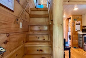 Wooden staircase with handrails in a cozy cabin on Just Wandering Lane, leading up from the kitchen and laundry area.
