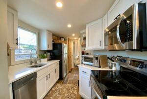 Modern kitchen on Just Wandering Lane with white cabinets, stainless steel appliances, and a window above the sink.