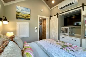Cozy bedroom on Just Wandering Lane with floral bedding, wall art, TV, and a barn door leading to the bathroom.