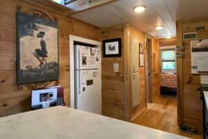 Cozy wooden kitchen and hallway on Just Wandering Lane, with wall art, fridge, and a view into a floral bedroom.