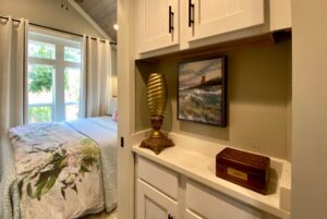 A cozy bedroom on Just Wandering Lane with floral bedding, a window view, and a shelf with charming decor.