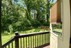 View from Just Wandering Lane: an open door to a porch, green backyard, and red chairs among the trees.