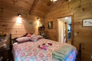 Cozy wooden bedroom on Just Wandering Lane with a patterned bedspread, pillows, wall art, and soft lighting.