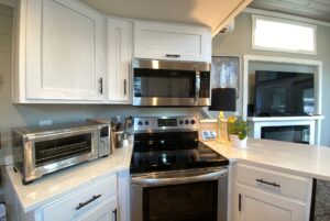 Modern kitchen on Just Wandering Lane with stainless steel stove, microwave, toaster oven, and white cabinets.