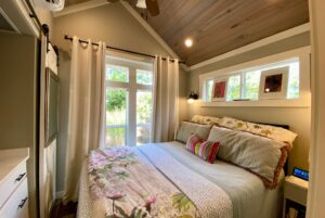 Small cozy bedroom on Just Wandering Lane with a large window, floral bedding, and three framed photos above the bed.