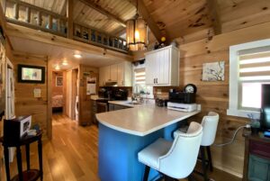 Cozy wooden kitchen with white cabinets, blue island, and bar stools in a cabin-style home on Just Wandering Lane.