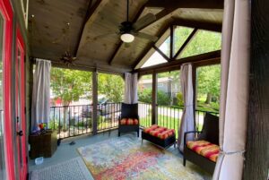 Screened porch on Just Wandering Lane with two cushioned chairs, colorful rug, and ceiling fan overlooking a green yard.