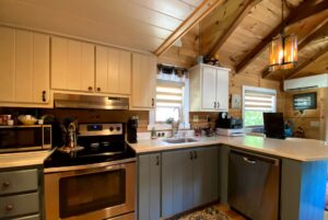 Cozy kitchen on Just Wandering Lane with wood walls, stainless appliances, white cabinets, and a window above the sink.