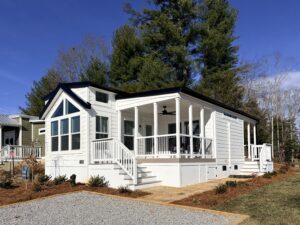 Tiny Home with a large front porch and steps, surrounded by trees and a gravel walkway.