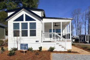 White tiny house with porch, large windows, and a sign that reads 129 Misty Knoll Way Lot #179 in front.