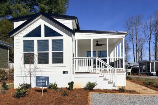 White tiny house with porch, large windows, and a sign that reads 129 Misty Knoll Way Lot #179 in front.