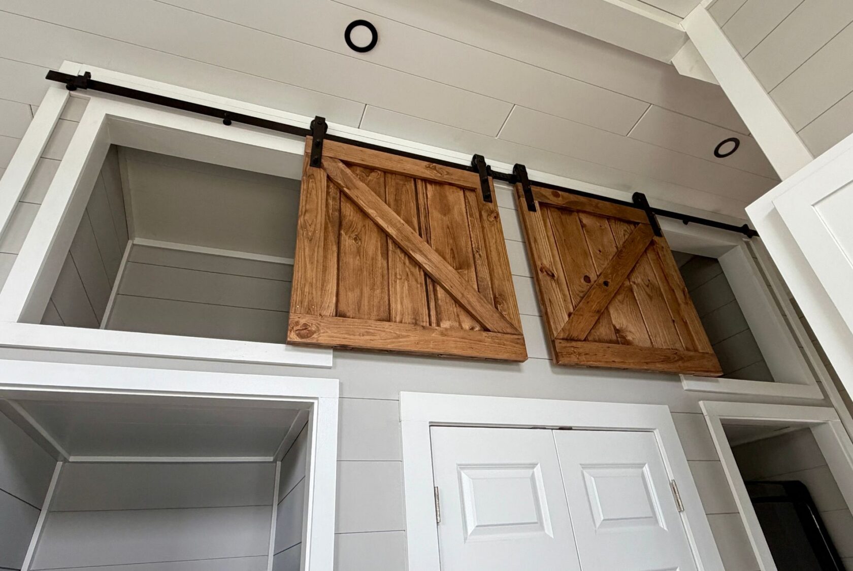 Two wooden sliding barn doors on a track above white double closet doors at 124 Misty Knoll Way.