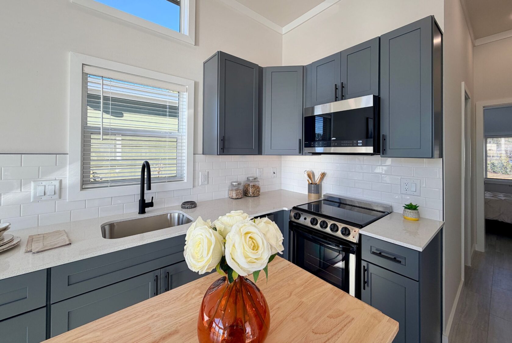 Modern kitchen with gray cabinets, stainless appliances, and white roses on a wooden island.