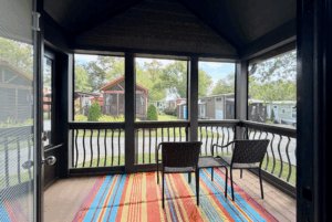 Screened porch at Two Swans Lane with two chairs and a table on a colorful rug, overlooking cabins and trees.