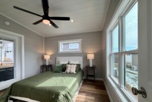 Bedroom at 124 Misty Knoll Way with green bedding, large windows, ceiling fan, and bedside tables with lamps.