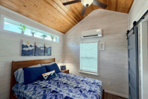 Cozy Skipping Stone Lane bedroom with wood ceiling, blue bedding, AC, plants, mountain art, and a barn door.