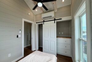 Small, modern bedroom at 124 Misty Knoll Way with light gray walls, sliding barn door, ceiling fan, and built-in drawers.