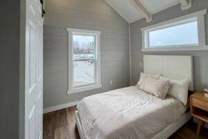 Small bedroom at 124 Misty Knoll Way with a white bed, wooden nightstand, and large window showing an outdoor view.