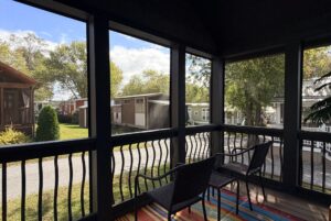 Two chairs on a screened porch overlook sunny Two Swans Lane, lined with tiny houses on a bright day.