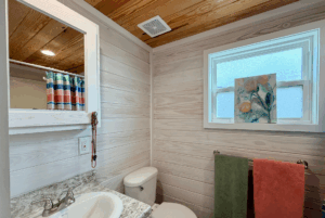 Small bathroom on Skipping Stone Lane with a sink, toilet, colorful towels, and floral art on the window ledge.
