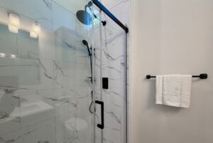 Modern shower with glass door, marble tile walls, black fixtures, and a white towel on the rack.