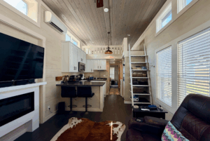 Modern tiny house interior at Two Swans Lane with a small kitchen, bar stools, loft, and large windows for natural light.
