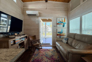 A cozy living room at 44 Skipping Stone Lane with a sofa, rocking chair, TV, and door to a sunny porch outside.