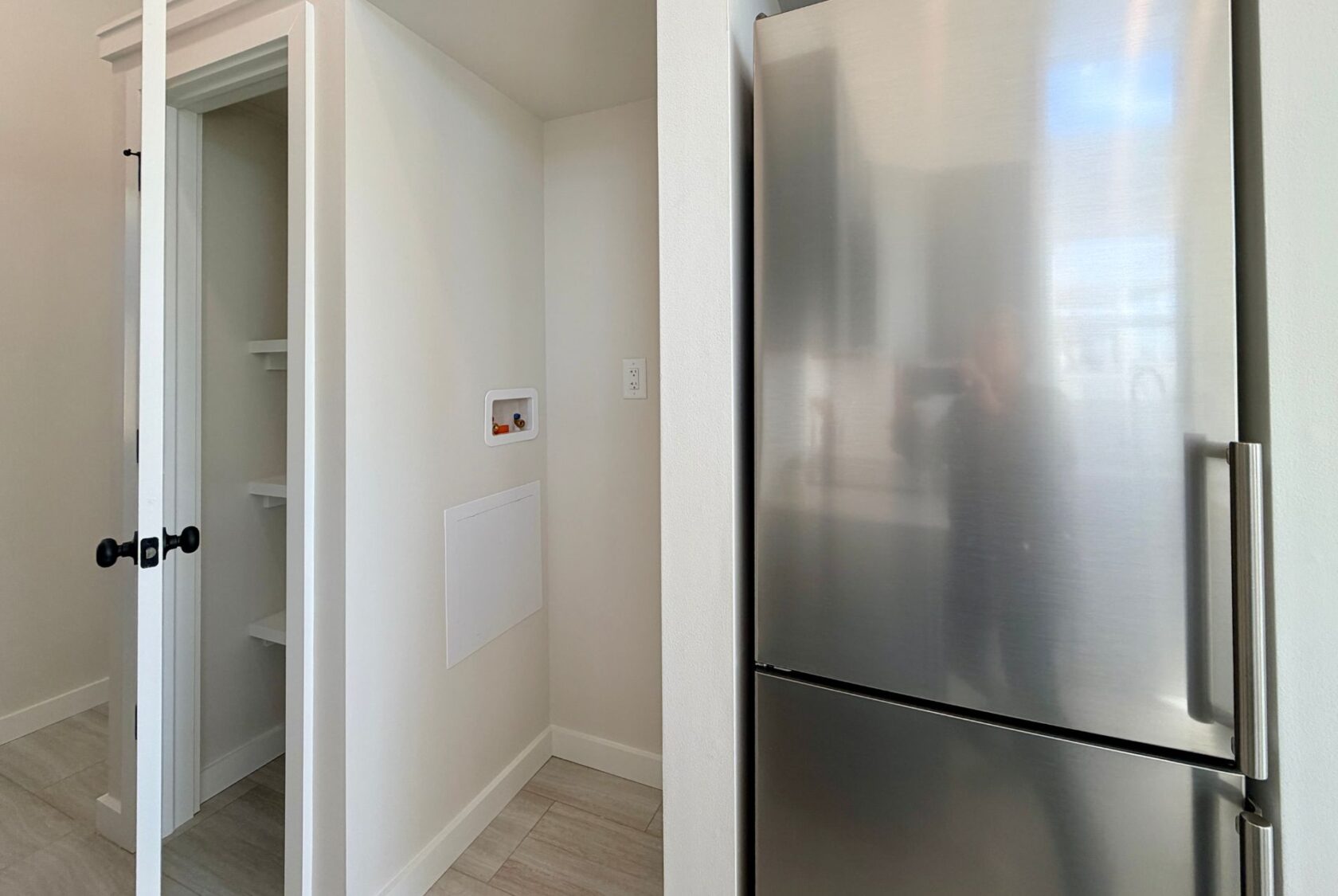 A stainless steel fridge beside an open closet with white shelves in a modern, bright room.