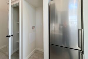 A stainless steel fridge beside an open closet with white shelves in a modern, bright room.