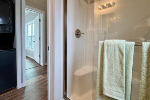 A glass shower with towels on the door, near laundry and an open doorway, brightens 124 Misty Knoll Way.