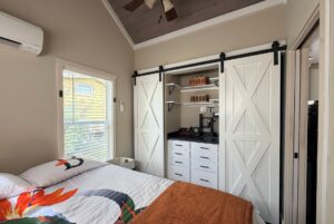 Bright bedroom at Two Swans Lane with a bed, window, and an open closet featuring white barn doors and organized shelves.