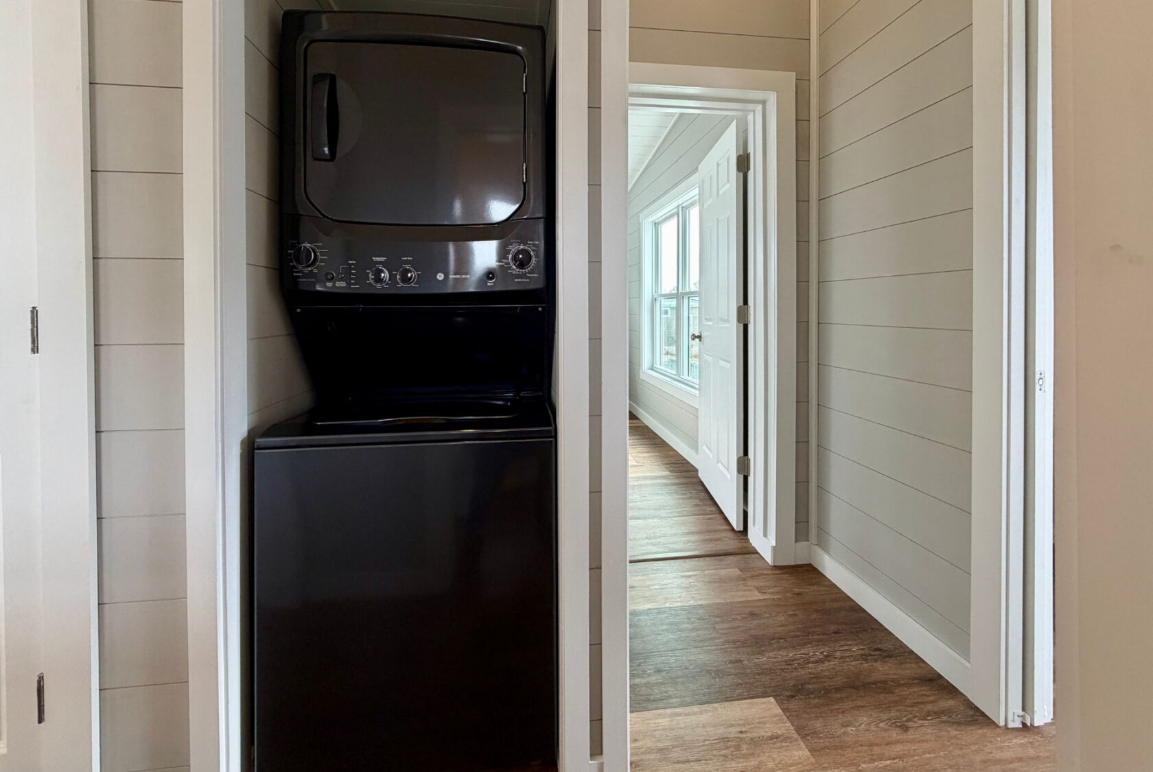Black stacked washer and dryer in a small laundry closet at 124 Misty Knoll Way, next to a hallway with wood flooring.