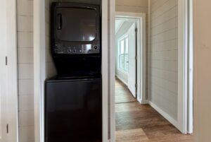 Black stacked washer and dryer in a small laundry closet at 124 Misty Knoll Way, next to a hallway with wood flooring.