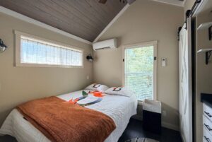 Cozy bedroom at Two Swans Lane with a bed, orange blanket, large windows, and wall air conditioner.