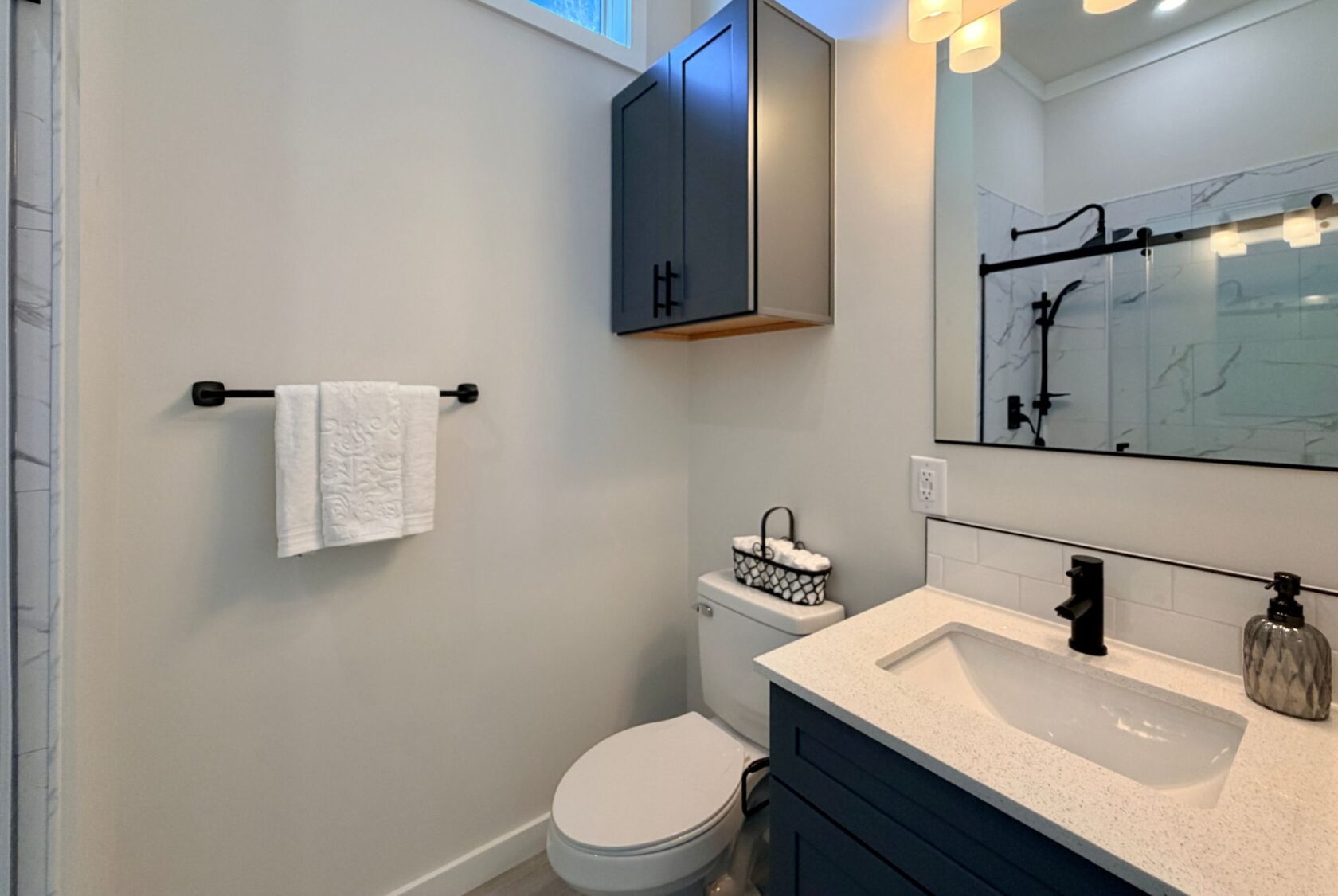 Modern bathroom with blue cabinets, towel rack, toilet, and a white countertop sink.