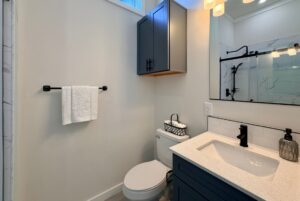 Modern bathroom with blue cabinets, towel rack, toilet, and a white countertop sink.