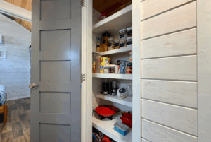 Small pantry on Skipping Stone Lane with gray door, shelves of food, appliances, and cookware in a cozy home.