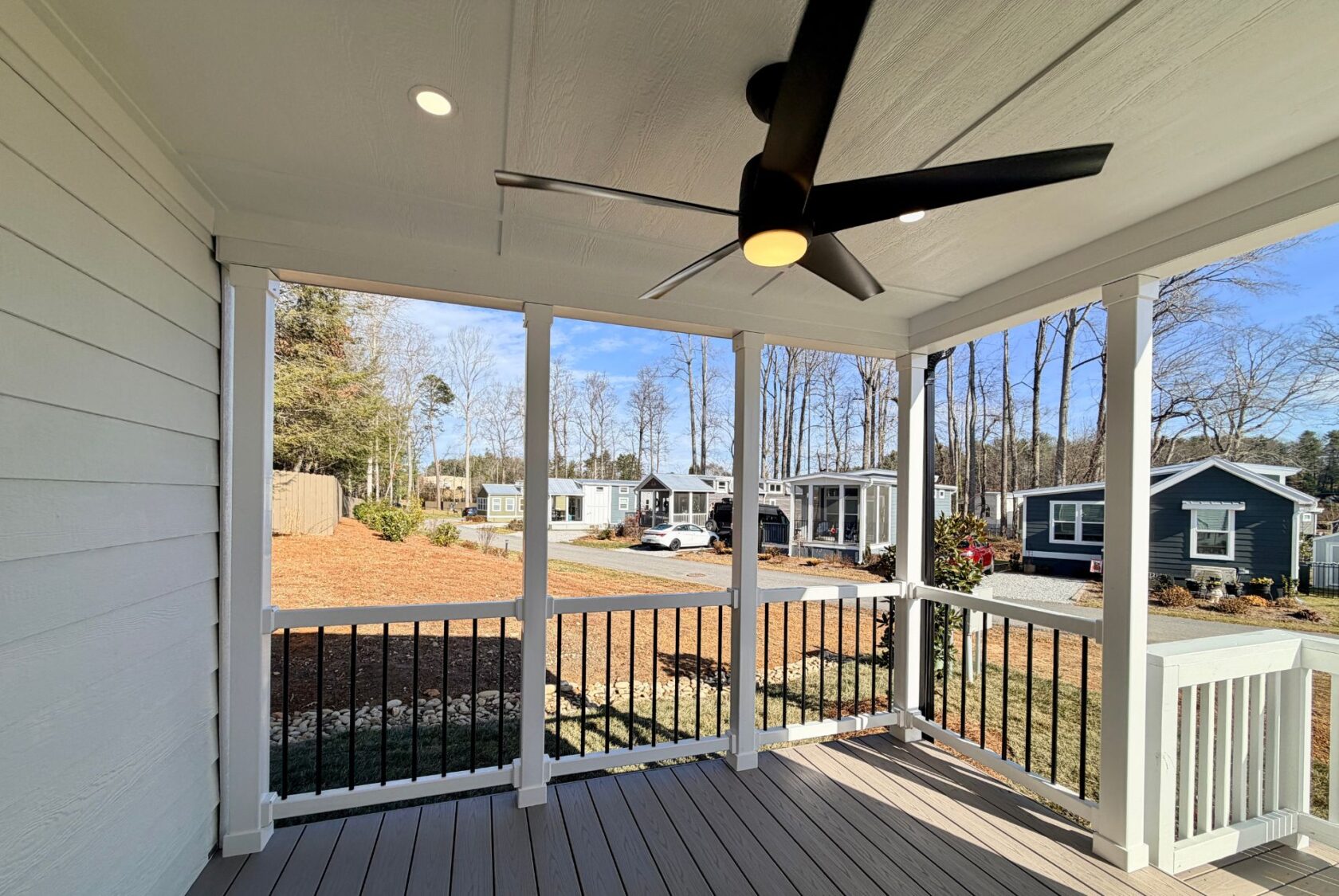Covered porch with ceiling fan at 129 Misty Knoll Way overlooks yard and several small homes on a sunny day.