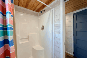 White shower with built-in seat, striped curtain, and wood ceiling brighten this Skipping Stone Lane bathroom.