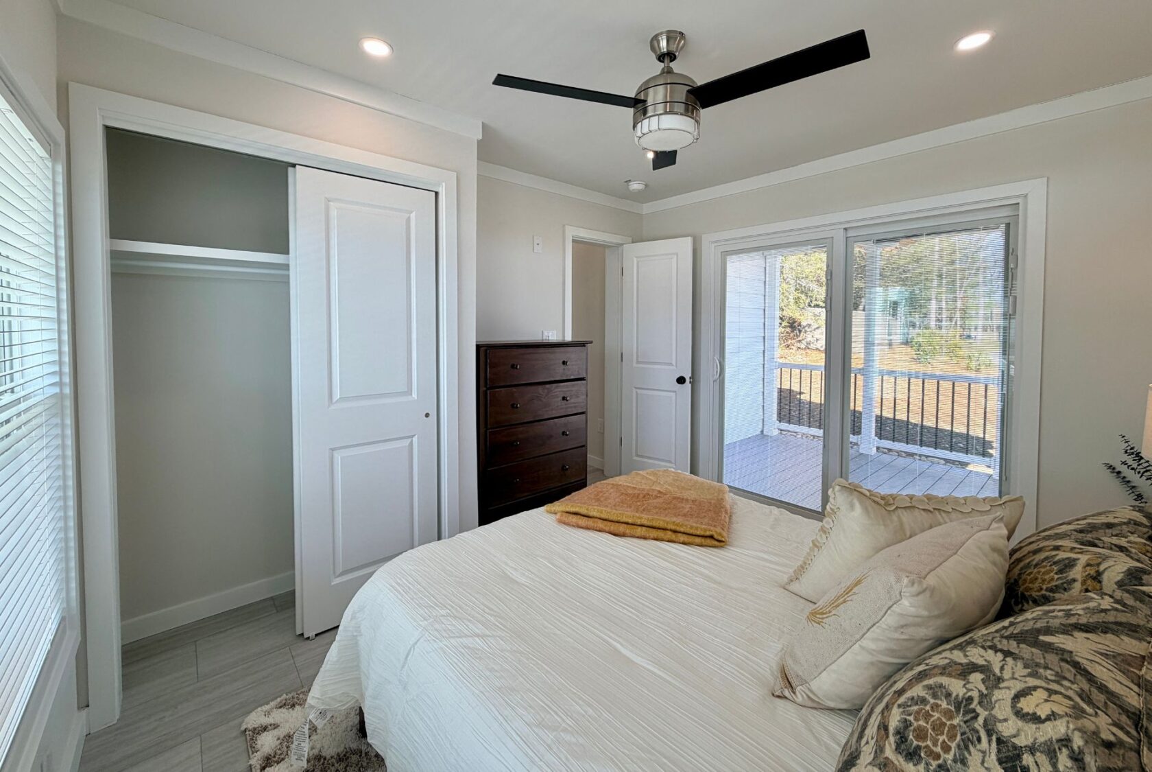 Bright bedroom with a bed, dresser, closet, ceiling fan, and glass doors to the deck.