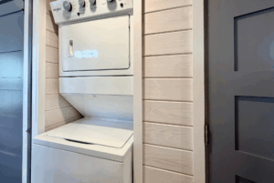 Stacked white washer and dryer unit in a small laundry nook at 44 Skipping Stone Lane with light wood panel walls.