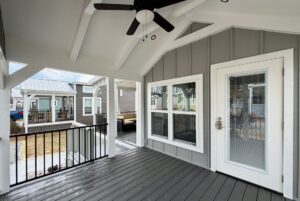 Covered porch at 124 Misty Knoll Way with a ceiling fan, gray siding, white trim, and railing overlooking similar houses.
