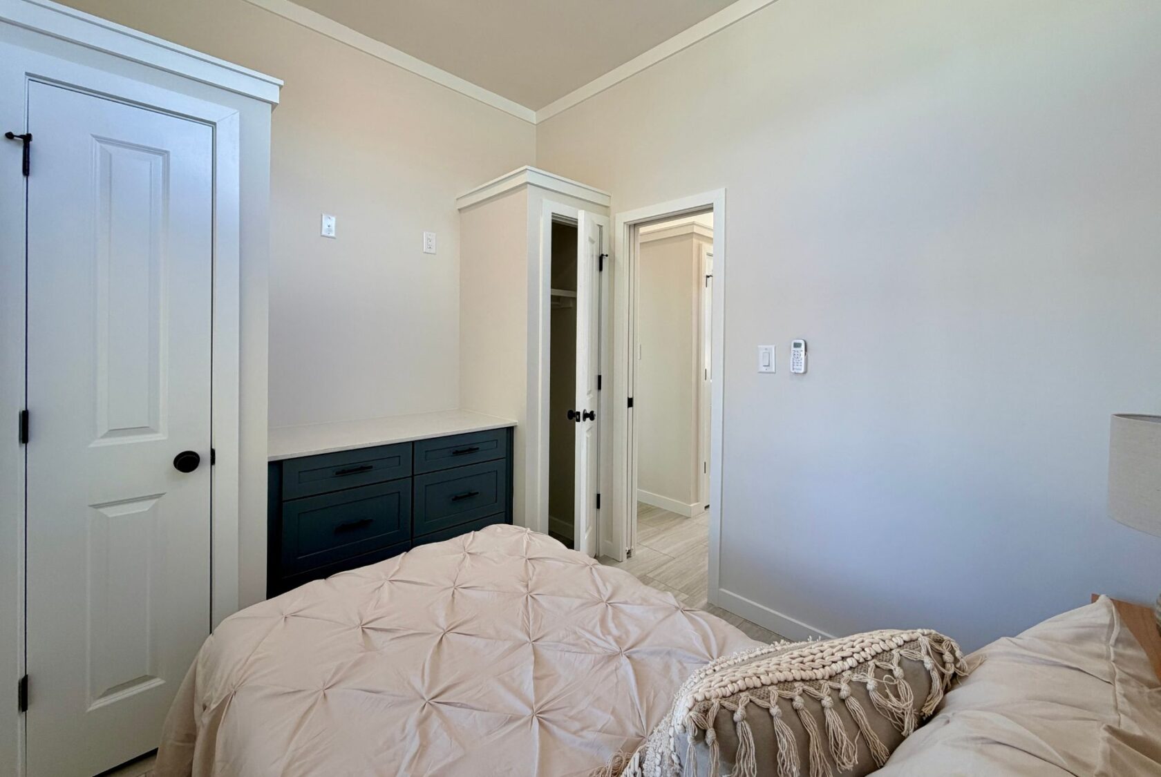 Cozy small bedroom features a white bedspread, closet, dresser, and doors to the hallway.