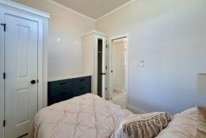 Cozy small bedroom features a white bedspread, closet, dresser, and doors to the hallway.