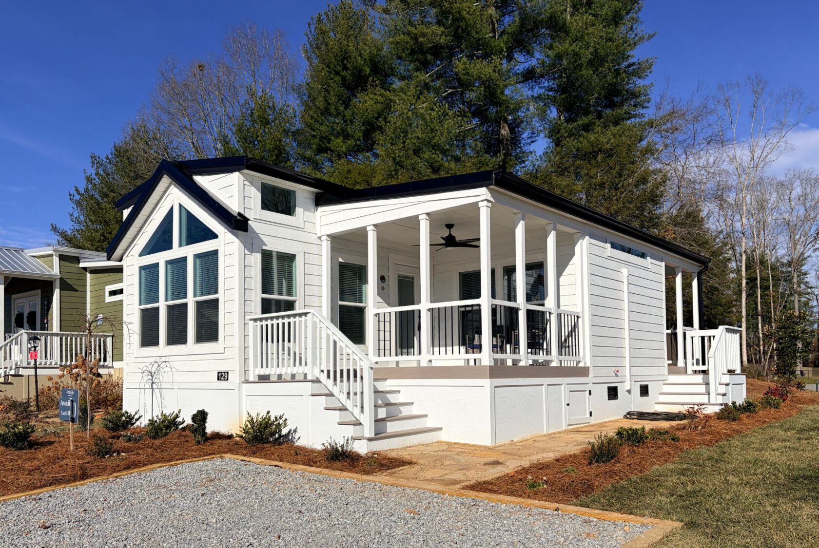 Modern white tiny house at 129 Misty Knoll with large windows, front porch, and landscaped yard under a clear blue sky.