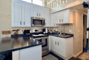 A small, modern kitchen on Two Swans Lane with white cabinets, black countertops, and stainless steel appliances.